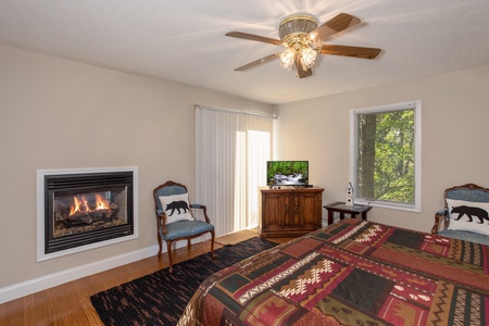 Bedroom with an in-wall fireplace, sitting area, TV, and deck access at Into the Woods, a 3 bedroom cabin rental located in Pigeon Forge