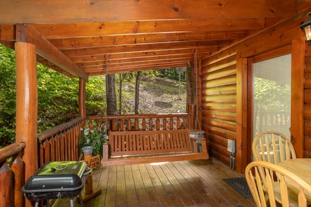 Covered porch with swing, dining space, and a charcoal grill at Dreams Do Come True, a 1-bedroom cabin rental located in Pigeon Forge