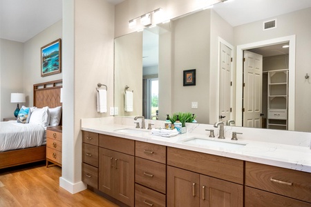 - Elegant bathroom with dual vanity sinks set in white countertops and warm wood cabinetry - Large mirror and bright lighting create a fresh and functional space for daily routines - Modern fixtures and thoughtful touches enhance the overall spa like feel