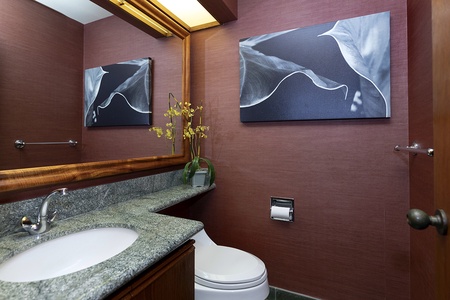 - Elegant half bath with granite countertop and warm wood cabinetry design - Mocha toned walls and framed artwork create a refined, stylish look - Orchid arrangement adds a fresh, tropical touch to the space