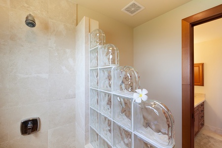 Guest Bath- Walk in shower accented with glass block wall for light and privacy   - Neutral toned tile and sleek fixtures create a clean, modern aesthetic   - Fresh tropical flower detail adds a welcoming island inspired touch