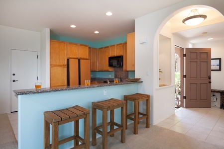- Relaxed seating at the bar makes this kitchen ideal for quick bites or happy hour chats - Modern appliances, wood cabinets, and ocean blue walls create a cheerful backdrop - Open archway leads to the breezy front entry with natural light streaming in