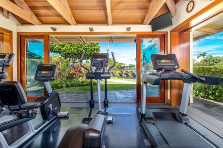 Stay active in your private fitness room with stunning garden views through open glass doors, where natural tropical beauty meets modern exercise equipment under warm wood beam ceilings.