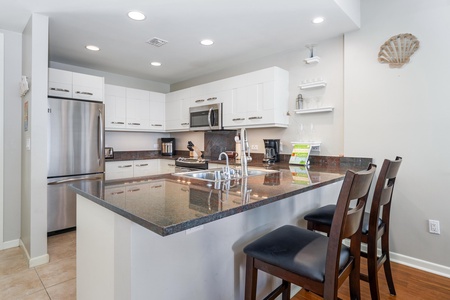 - Sleek granite countertops wrap around a modern kitchen with stainless appliances - Bar stools offer the perfect perch for snacks, coffee, or casual conversation - Clean white cabinetry and under cabinet lighting brighten the space beautifully