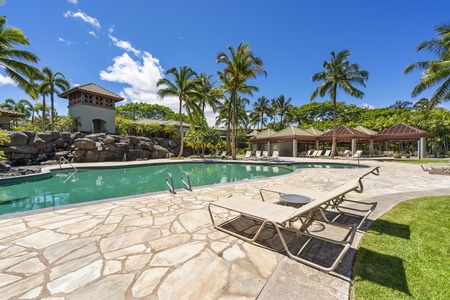 Large resort style pool with stone deck surrounded by swaying palm trees.