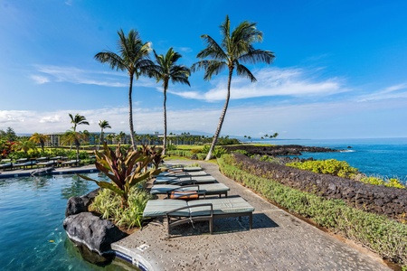 Oceanfront pool deck with tropical palms overlooking volcanic coastline and azure waters.