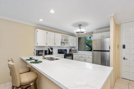 - Bright kitchen with white cabinets, quartz counters, and stainless appliances - Window over the sink frames beautiful tropical greenery as you prep meals or snacks - Barstools and pendant light make this space as stylish as it is functional