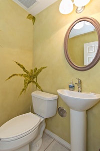 - Freshen up in a charming powder room with a sleek pedestal sink and round mirror   - Soft yellow walls feature a delicate fern mural adding a touch of nature   - Bright and functional space ideal for quick refreshes during your stay