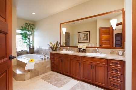 - Bathroom featuring a double vanity with rich wood cabinetry & granite countertop   - Large framed mirror reflects warm lighting, enhancing the inviting atmosphere   - Deep soaking tub in the corner offers a peaceful retreat with spa like relaxation