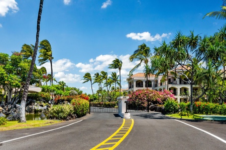 Tropical entrance to an exclusive gated community featuring lush palm trees, vibrant flowering gardens, and elegant architecture.