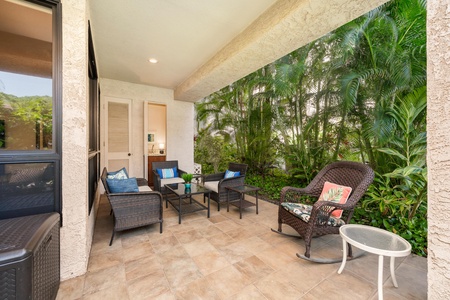 Sink into plush wicker seating surrounded by lush tropical palms on your private covered patio, perfect for morning coffee or evening relaxation.