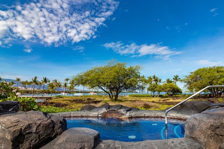 A naturally-styled pool framed by volcanic rock, with a serene coastal landscape stretching toward the ocean beyond palm-lined greens.