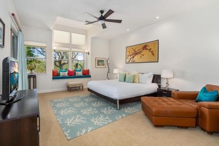 - Spacious bedroom with modern king bed, soft toned walls, and bright natural light - Cozy bench nook framed by tall windows and vibrant pillows - Ceiling fan, coral pattern rug, and leather lounger add comfort and charm