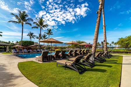 Row of sun loungers shaded by umbrellas beside the tropical poolside.