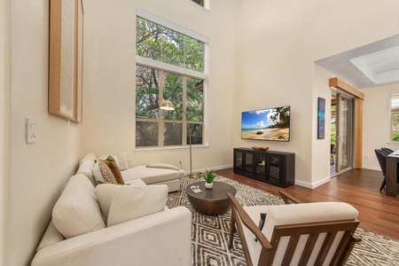 Unwind in your elegant living room with plush seating, warm wood floors, and tropical garden views through expansive windows.