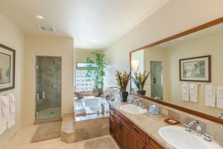 - Spacious bathroom with dual sinks set in sleek granite, framed by warm wood cabinetry   - Glass enclosed shower pairs with a soaking tub for quick refreshes & long soaks   - Decorative greenery & elegant accents create a serene, rejuvenating environment