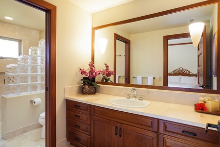 - Bathroom with single vanity set in warm wood cabinetry and marble top   - Large mirror framed in wood reflects the soft ambient wall lighting   - Direct access to shower and toilet area enhances convenience and privacy