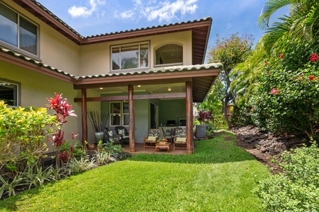 Covered patio with outdoor seating opens to a vibrant lawn and garden space.