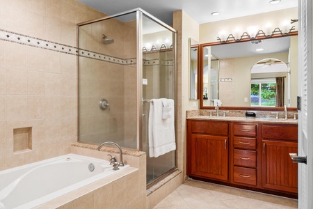 En suite primary bathroom with dual sinks, granite countertops, bathtub, and walk in shower
