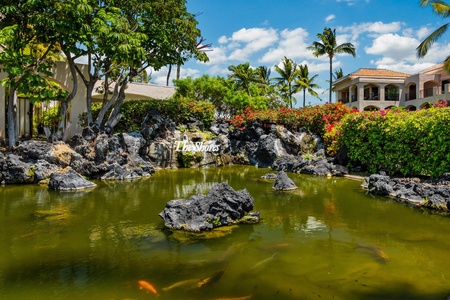 A tranquil koi pond surrounded by volcanic rock formations, lush tropical gardens, and swaying palms welcomes guests at the property's scenic entrance area.