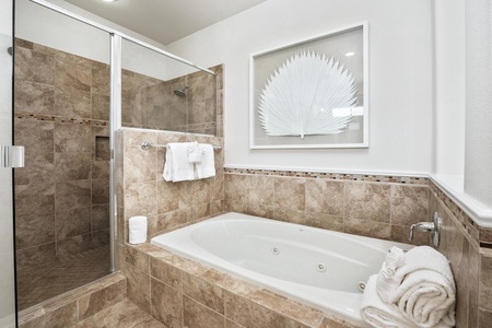 Unwind in your luxurious spa-style bathroom with a jetted soaking tub and separate glass shower featuring beautiful stone tilework.