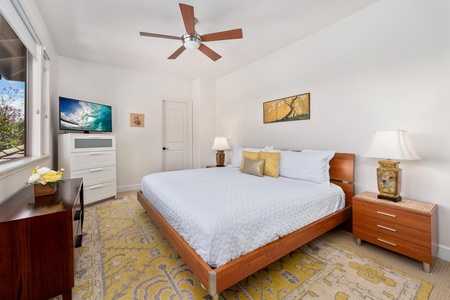 - Spacious bedroom with a king bed, cozy lighting, and calming artwork - Soft yellow and white color palette sets a tranquil tone - Wall mounted TV and dresser provide both entertainment and storage