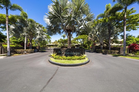 Gated roundabout entrance with tropical palm landscaping and a welcoming community sign.