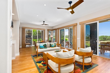 - Spacious living room with vibrant rug & modern ceiling fans adding flair & comfort - Stylish sliding doors bring in natural light & connect to outdoor lounging areas - Cozy arrangement perfect for relaxing while enjoying surrounding tropical scenery