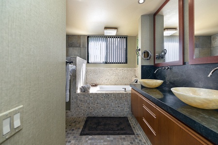 Bright bathroom with soaking tub, dual sinks, and stone counters.
