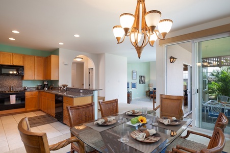 - Glass top dining table comfortably seats six beneath a glowing chandelier for stylish meals - Open floor plan leads into the kitchen and bright hallway beyond - Enjoy meals with a view or step out to the patio through the nearby sliding glass door