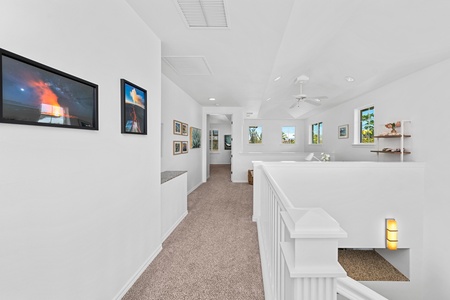 - Bright upstairs hallway featuring carpet flooring and walls adorned with vibrant artwork - Windows bring in natural light creating an open and airy walkway - Leads to bedrooms and a lounge making movement through the home seamless