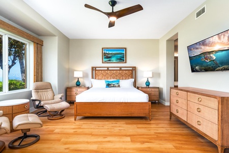 - King bedroom with warm wood furniture and matching dresser for added storage space - Framed artwork and soft lighting create a calm and inviting atmosphere - Ceiling fan and large TV add comfort and convenience to the serene setting