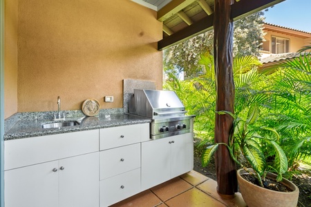 Outdoor kitchen features a stainless grill, granite counters, and sink.