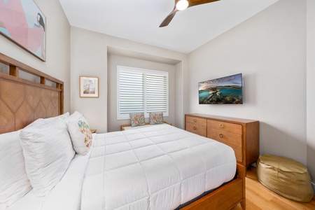 - Guest bedroom with cozy bed framed in warm wood and neutral bedding for a calm feel - Wall mounted TV offers entertainment while bench seating beneath window adds charm - Shuttered window allows light control and privacy for a comfortable stay