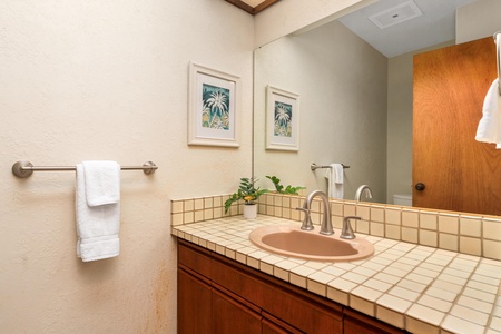 Freshen up in your private bathroom featuring warm tile counters, tropical artwork, and fresh towels ready for your stay.