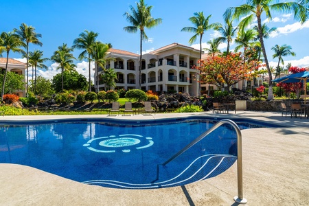 The resort features a sparkling pool surrounded by lush tropical palms, vibrant gardens, and elegant Mediterranean-style buildings with tiled roofs, creating an idyllic Hawaiian retreat.