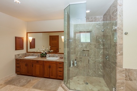 - Elegant bathroom with double vanity and rich wood cabinetry for storage - Stylish glass shower with marble tile adds a touch of modern style - Large framed mirror reflects warm lighting for a spa like atmosphere