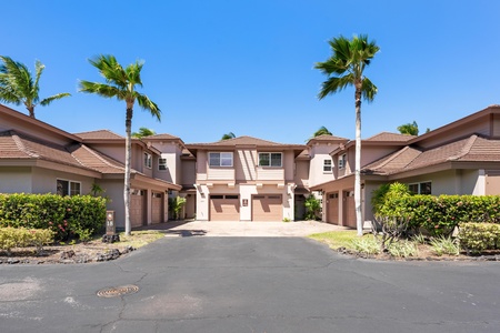 Two-story Mediterranean-style villa with private garage in a landscaped community beneath swaying palm trees and clear blue skies.
