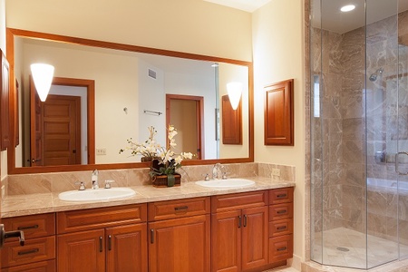 - Elegant bathroom with double vanity and granite countertop framed in wood   - Large mirror and soft wall lighting enhance the room’s warm, polished style   - Walk in glass shower adds a modern touch for a spa like bathing experience