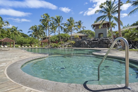 Resort-style swimming pool surrounded by tropical palm trees and landscaped grounds with poolside seating areas.