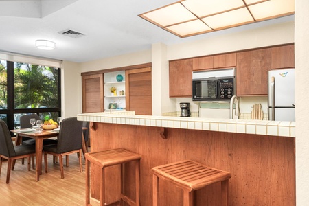 Your fully equipped kitchen opens to a dining area where you can cook and gather, with warm wood finishes and tropical views.