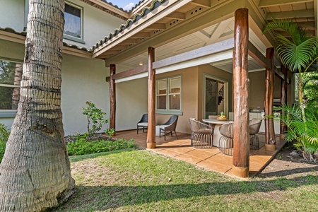 Tropical villa exterior featuring a covered patio with wooden beams, outdoor seating, and lush palm landscaping.