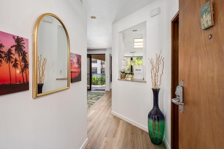 Step through your private entrance into a bright, welcoming space adorned with tropical artwork and warm wood floors that flow toward sunlit rooms beyond.
