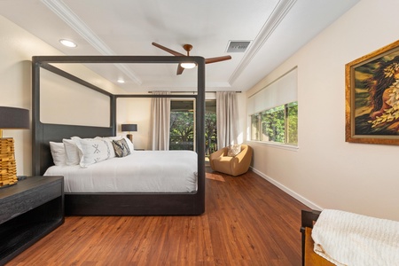 Unwind in your serene bedroom featuring a striking canopy bed, rich hardwood floors, and garden views streaming through bright windows.