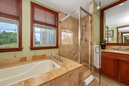 Unwind in your spacious bathroom featuring a deep soaking tub, walk-in glass shower, and warm tropical views through the window. Rich wood accents and earthy tones create a relaxing spa-like retreat.