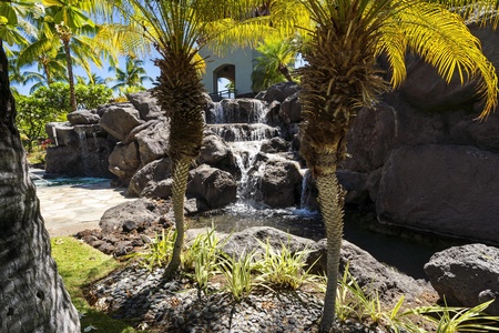 A tropical waterfall cascades over volcanic rocks beneath swaying palms, creating a serene lagoon setting in this resort paradise.