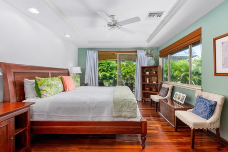 - Spacious bedroom with king bed, hardwood floors, and ceiling fan - Sliding glass doors lead to a private balcony surrounded by greenery - Large window fills the room with natural light and scenic views