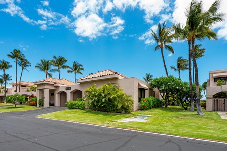 Corner unit with manicured lawn and swaying palm trees under blue skies.