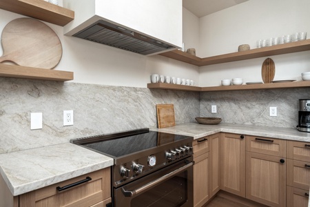 Your modern kitchen features granite counters, gas stove, and open shelving stocked with dishes for memorable meals.