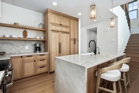 Your chef-worthy kitchen awaits with marble waterfall island, warm wood cabinetry, and pendant lights creating perfect ambiance for cooking.